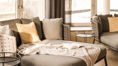 Gemütliche Sitzecke mit grauem Sofa, Kissen und Buch am Fenster