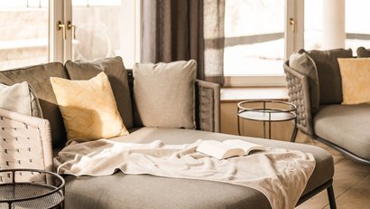 Gemütliche Sitzecke mit grauem Sofa, Kissen und Buch am Fenster