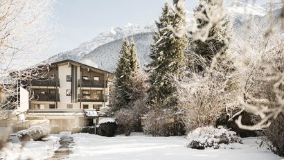 Schneebedecktes Haus und Bäume vor verschneiten Bergen im Winter