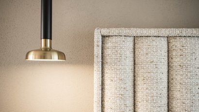 Goldene Wandlampe neben hellgrauem gepolstertem Kopfteil