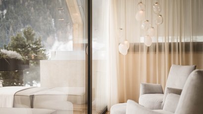 Gemütlicher Sessel und Fenster mit Blick auf Bäume und sanfte Vorhänge