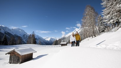 Paar wandert im verschneiten Bergtal bei klarem Himmel