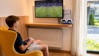 Junge spielt Videospiele auf Fernseher in gemütlichem Zimmer mit gelbem Sessel