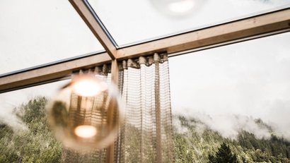 Blick durch Fenster auf nebeligen Wald mit Vorhang und Lichtquelle