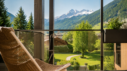 Balkon mit Stuhl und Blick auf grüne Berge und schneebedeckte Gipfel