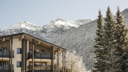 Moderne Unterkunft vor verschneitem Berg und Nadelbäumen