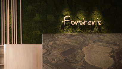 Forster's Logo an grüner moosbedeckter Wand mit Steinmarmor im Vordergrund