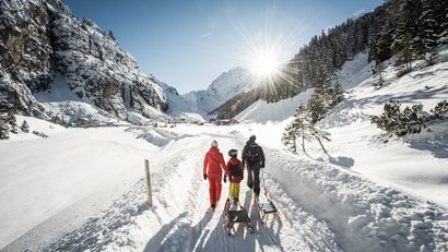 Familie mit Schlitten wandert im sonnigen Schneetal zwischen Bergen