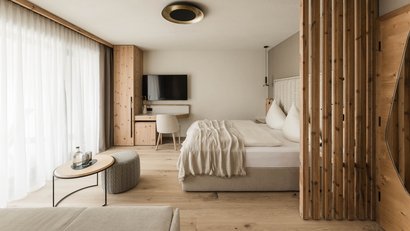 Helles Zimmer mit Doppelbett, Holzmöbeln und großem Fenster mit Vorhängen