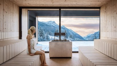 Frau in Sauna mit Blick auf verschneite Berglandschaft