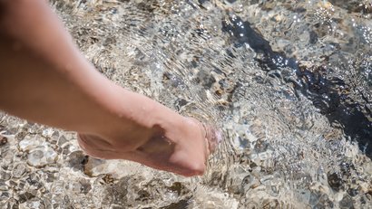 Fuß, der vorsichtig klares Wasser mit Kieselsteinen berührt