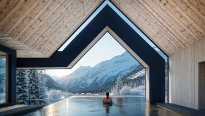 Person in Außenpool mit Blick auf verschneite Berge und Holzhaus