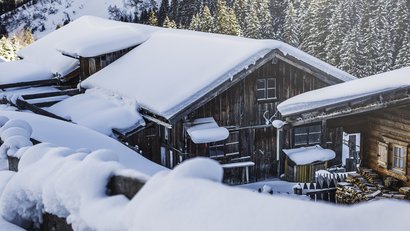 Verschneite Holzhütten in einem Bergwald bei Sonnenschein