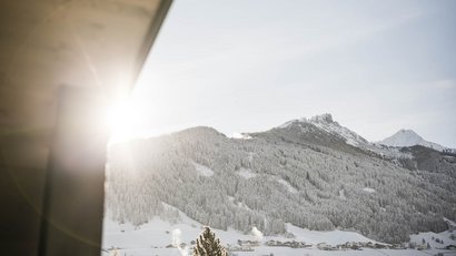 Sonniger Winterberg mit verschneiten Bäumen und Dorf im Tal
