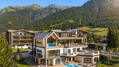 Modernes Hotel mit Außenpool vor bewaldeten Bergen bei Sonnenschein