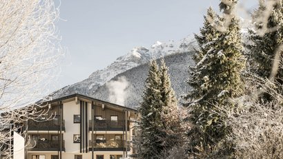 Modernes Haus im Winter mit schneebedeckten Bergen und Bäumen im Hintergrund