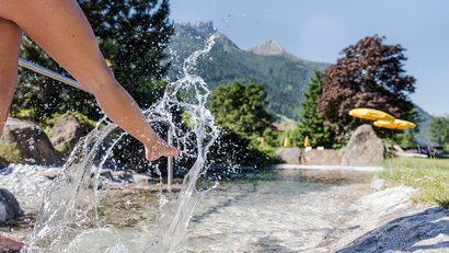 Beine spritzen Wasser in einem klaren Bach vor Bergkulisse