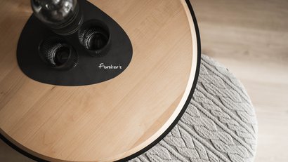 Ovale Holztischplatte mit schwarz-grauem Untersetzer und Gläsern