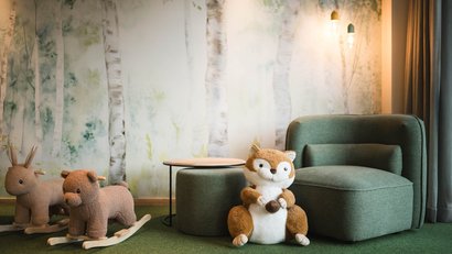 Kinderzimmer mit Kuscheltier, zwei Schaukeltiere und grünem Sessel