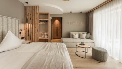 Modernes Schlafzimmer mit Bett, Sofa, kleinem Tisch und großem Fenster mit Vorhängen