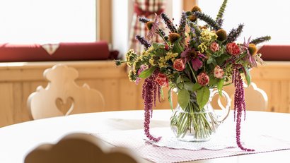 Bunter Blumenstrauß in klarem Glas auf rundem Holztisch im hellen Raum