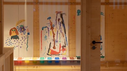 Blick durch Glastür auf Kinderkunst und bunte Farbflaschen im Raum