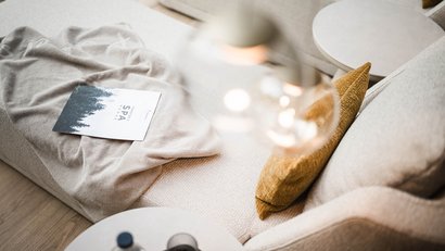 Bequemer Sessel mit Kissen, Decke und Spa-Menü auf beigem Sofa