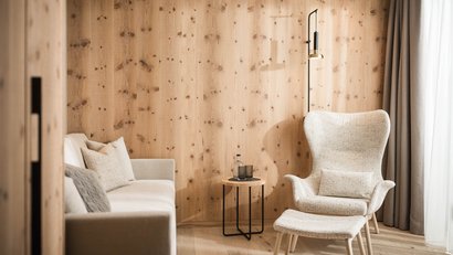 Gemütlicher Licht-Sessel und Sofa vor Holzpaneelwand im minimalen Wohnzimmer