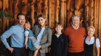 Mehrgenerationenfamilie steht vor Holzwand und lächelt in die Kamera