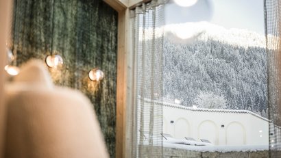 Blick durch Fenster auf schneebedeckte Berge und Gartenmöbel im Winter