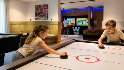 Kinder spielen Airhockey in einem modernen Spielzimmer mit Videospielen im Hintergrund