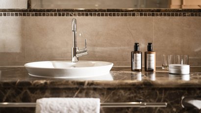 Moderner Waschtisch mit Wasserhahn und Pflegeprodukten auf Marmoroberfläche