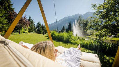 Frau entspannt auf Hängesessel im Garten mit Bergblick und Springbrunnen