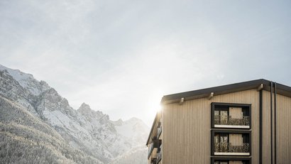 Holzgebäude mit Balkonen vor schneebedeckten Bergen im Sonnenlicht