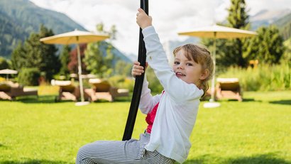 Kleines Mädchen spielt draußen auf einem Spielgerät im Garten