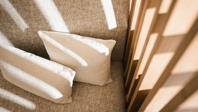 Sonnenlicht fällt auf zwei helle Kissen auf einem grauen Sofa neben Holz