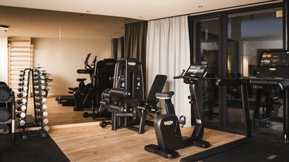 Fitnessraum mit Trainingsgeräten und Hanteln vor großem Spiegel