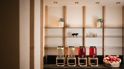 Vier Getränkespender auf Holzständern und Apfelkorb auf Marmorplatte