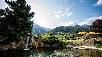 Berglandschaft mit Wasserfall, See und gelben Sonnenschirmen auf einer Wiese