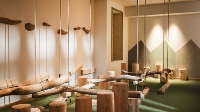 Ein natürlicher Indoor-Spielplatz mit hängenden Holzschaukeln und Baumstammstühlen