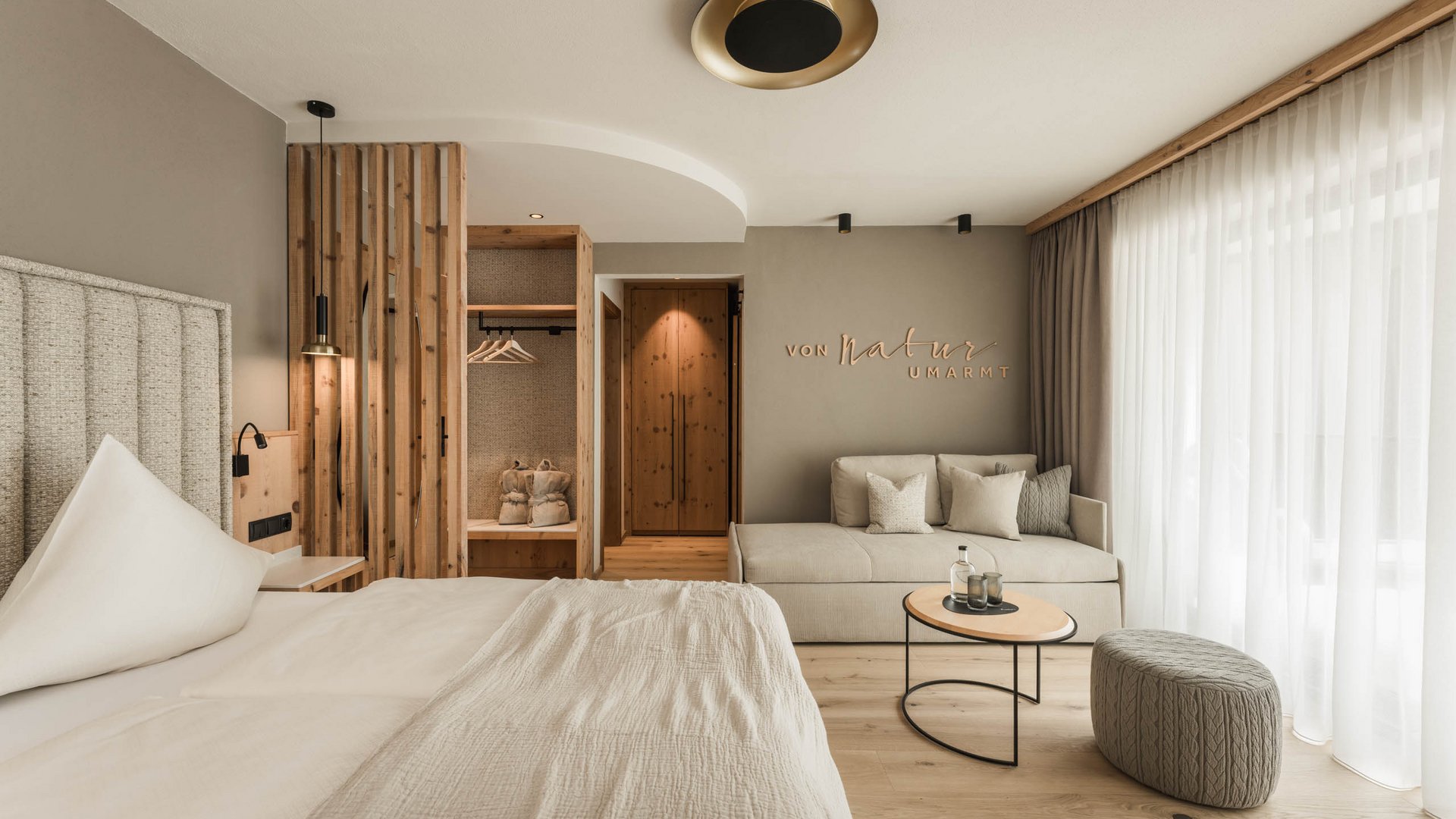 Helles Hotelzimmer mit Doppelbett, Sitzbereich, Holzelementen und großen Fenstern