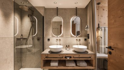 Modernes Badezimmer mit zwei Waschbecken, beleuchteten ovalen Spiegeln und Dusche