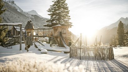 Verschneiter Spielplatz mit Holzhütten und Rutsche in Berglandschaft bei Sonnenlicht
