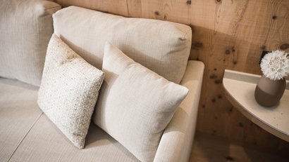 Beige Sofa mit zwei Kissen und Holzpaneelwand im Hintergrund