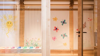 Kindergartenraum mit bunten Bildern von Sonne, Blumen und Schmetterlingen an der Wand