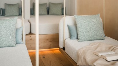 Weißer Sitzbereich mit grünen Kissen und offenem Buch auf Decke