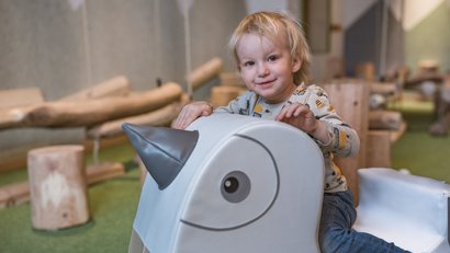 Kleines Kind sitzt auf einem Spielzeug-Einhorn im Innenbereich