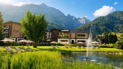 Hotel mit Liegestühlen und Teich vor Bergen bei sonnigem Wetter