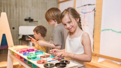 Drei Kinder malen fröhlich an einem Maltisch mit bunten Farben