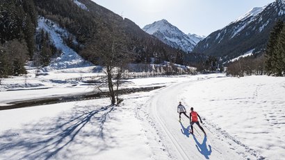 Zwei Langläufer auf schneebedeckter Strecke in bergiger Winterlandschaft